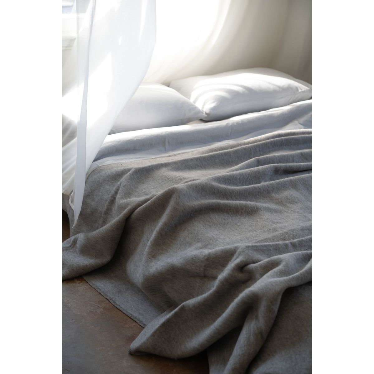 Gray blanket draped over a bed with white pillows in a softly lit room.