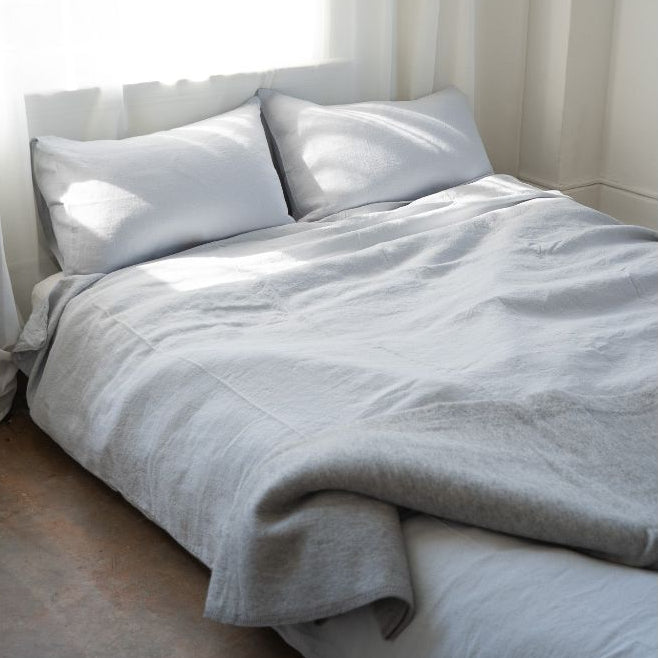 Neatly made bed with light gray bedding in a bright room.