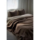 Brown blanket and pillows on a bed with light curtains in the background