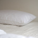 A close up of a white Somn Home luxury duck feather pillow insert cushion insert on a bed.